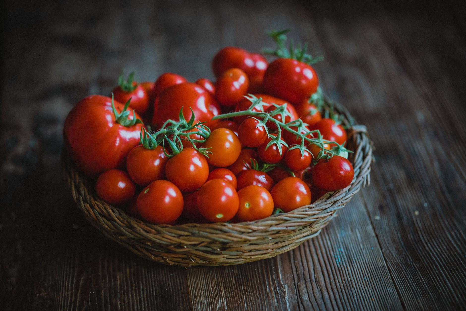 Vibrant basket of fresh red tomatoes on a rustic wooden table.