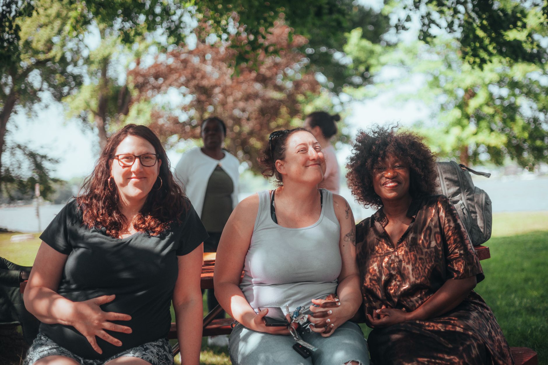 Group of diverse women sitting together in a park, smiling and enjoying a sunny day.